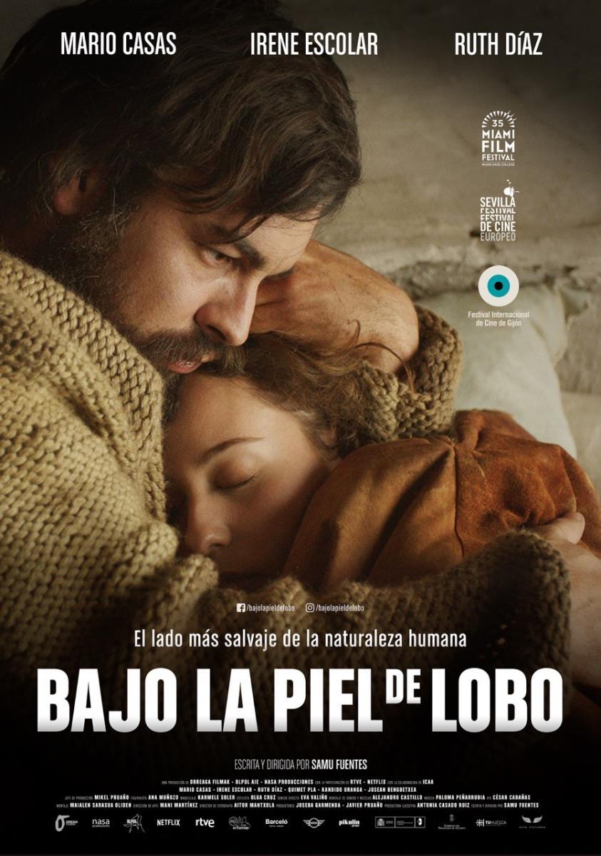 Cartel del largometraje Bajo la piel de lobo, en el que aparece Mario Casas con barba y pelo largo, vestido con un abrigo de punto gordo y abrazando a Irene Escolar.